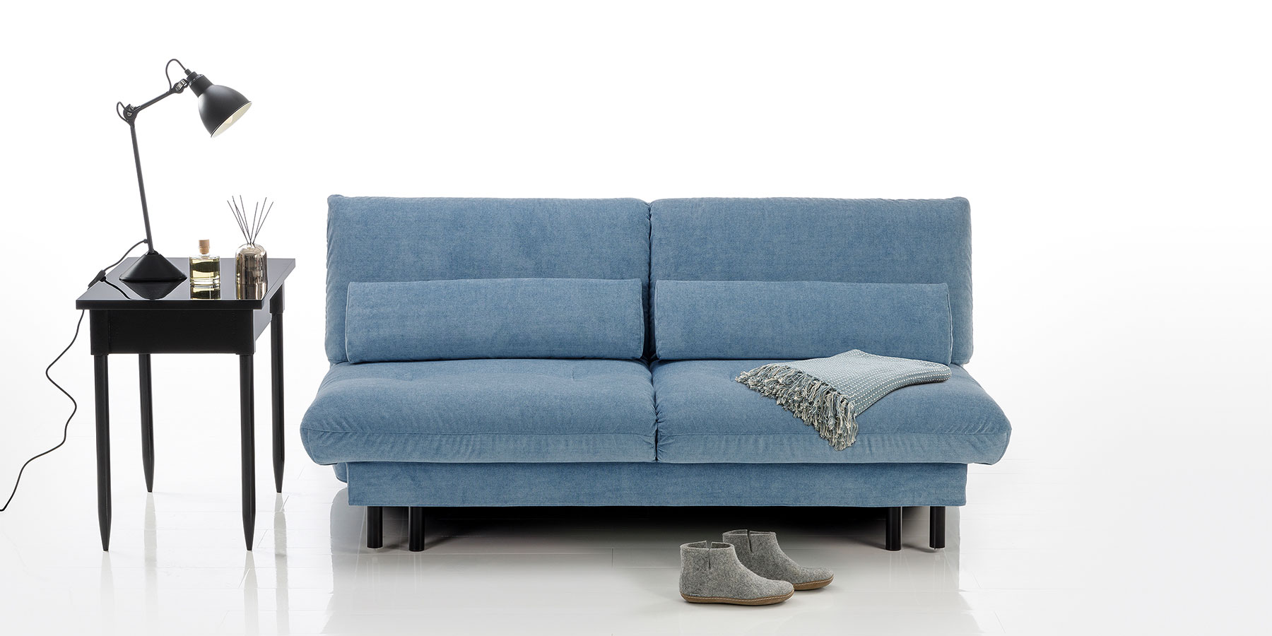 Bettsofa brühl quint Ein hellblaues Bettsofa mit schwarzen Metallfüßen. Das Sofa ist in der Mitte durch eine Teilungsnaht gegliedert.