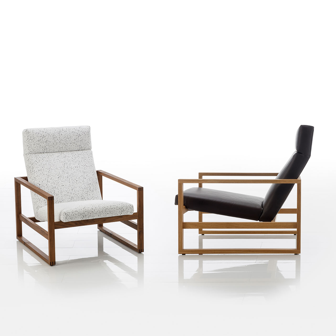 brühl grace wood 68111 Zwei Lounge-Sesse. mit nieriger Sitzhöhe. Die Gestelle sind aus Holz. Der linke Sessel ist mit einem weißen, strukturierten Stoff bezogen, der rechte Sessel ist mit schwarzem Leder bezogen.