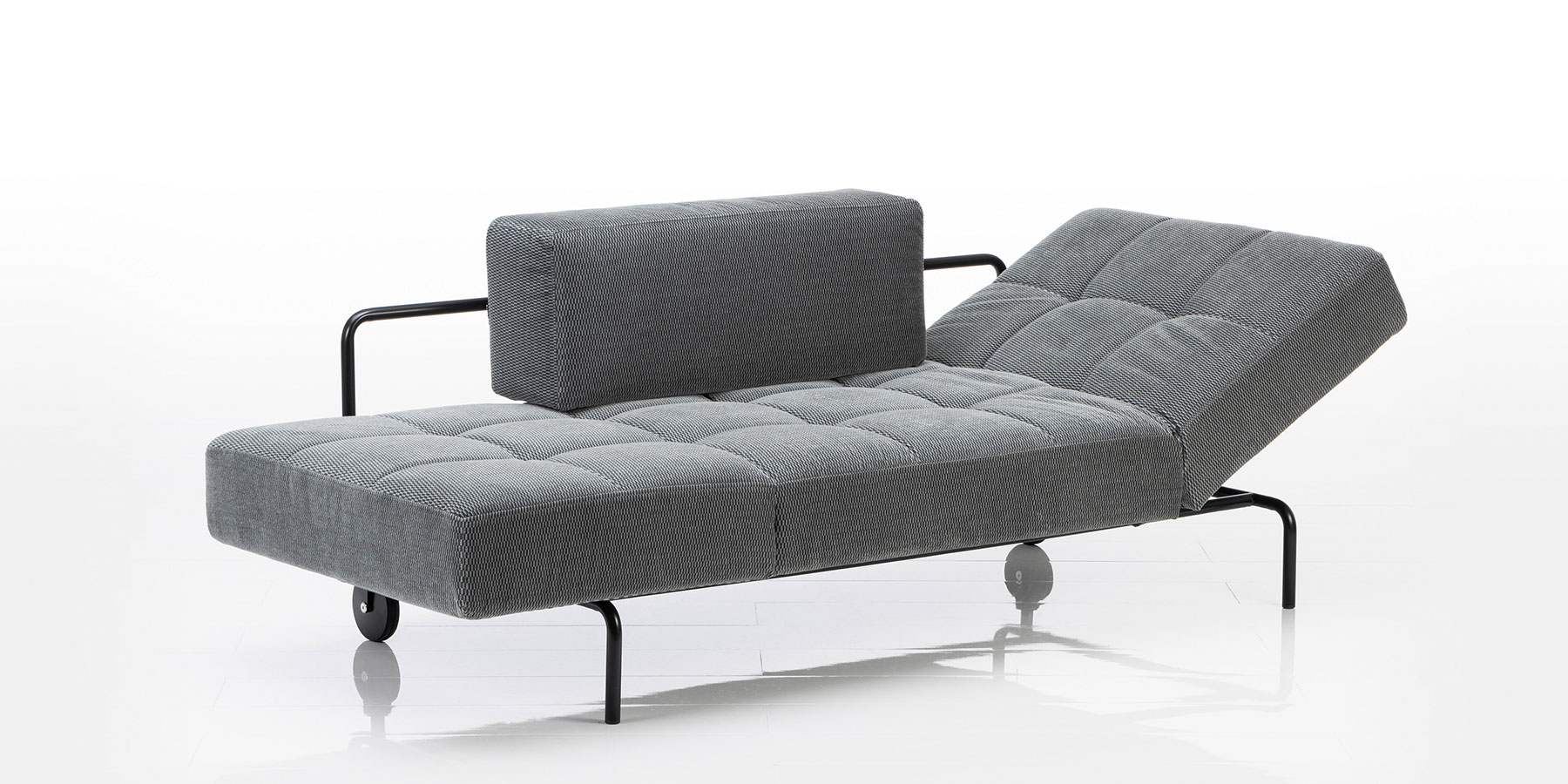 Recamieren und Openends von brühl stehen sowohl allein, lassen sich aber auch zu Garnituren kombinieren. Eine Recamiere mit schwarzem Untergestell. Das Polster ist gesteppt, das Rückenlehnkissen ist kubisch und hinten nur angelegt.