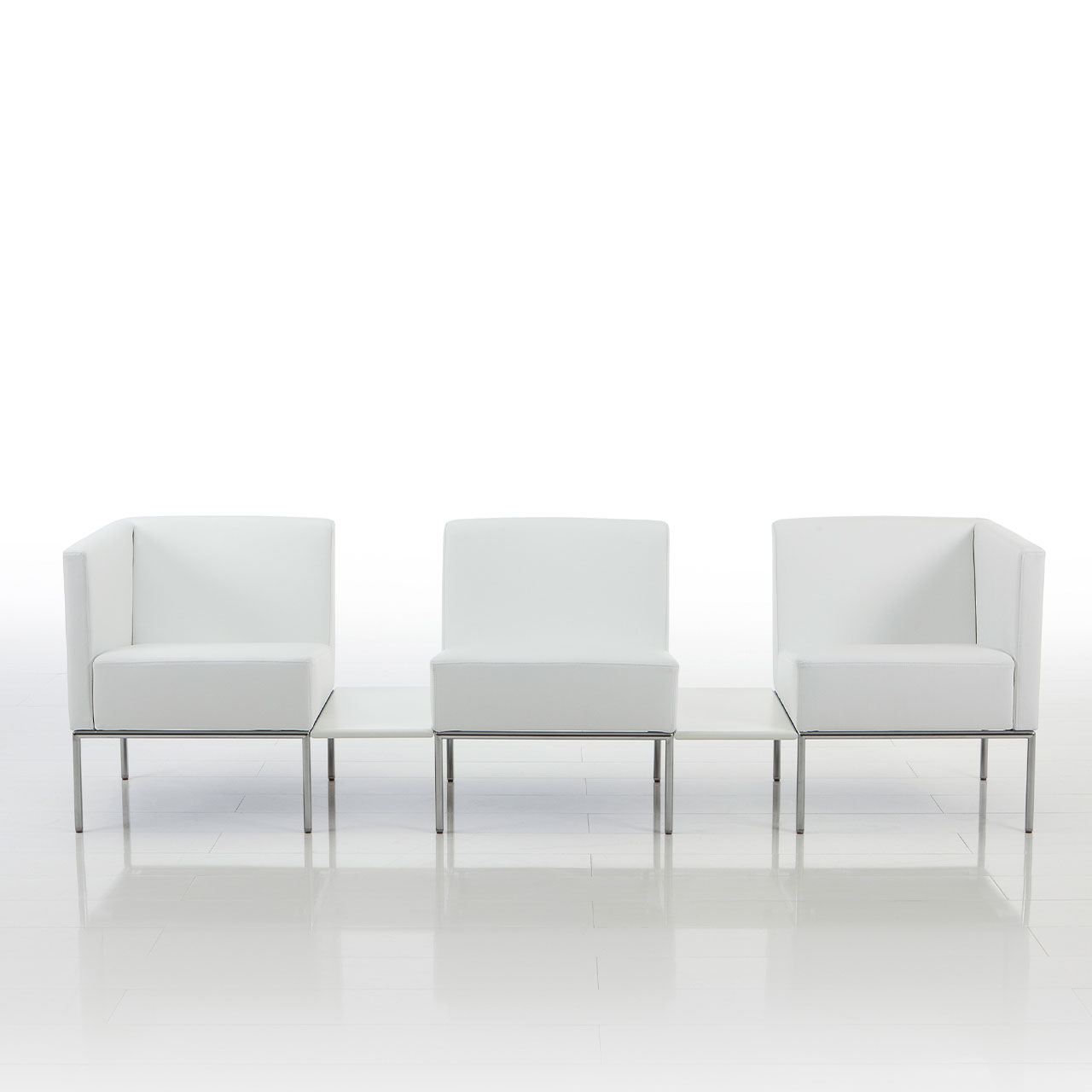 Gerade Sitzgruppe von brühl add1 bestehend aus drei Sesseln in weißem Stoff. Die Sessel sind durch rechteckige  Tablars miteinander verbunden.