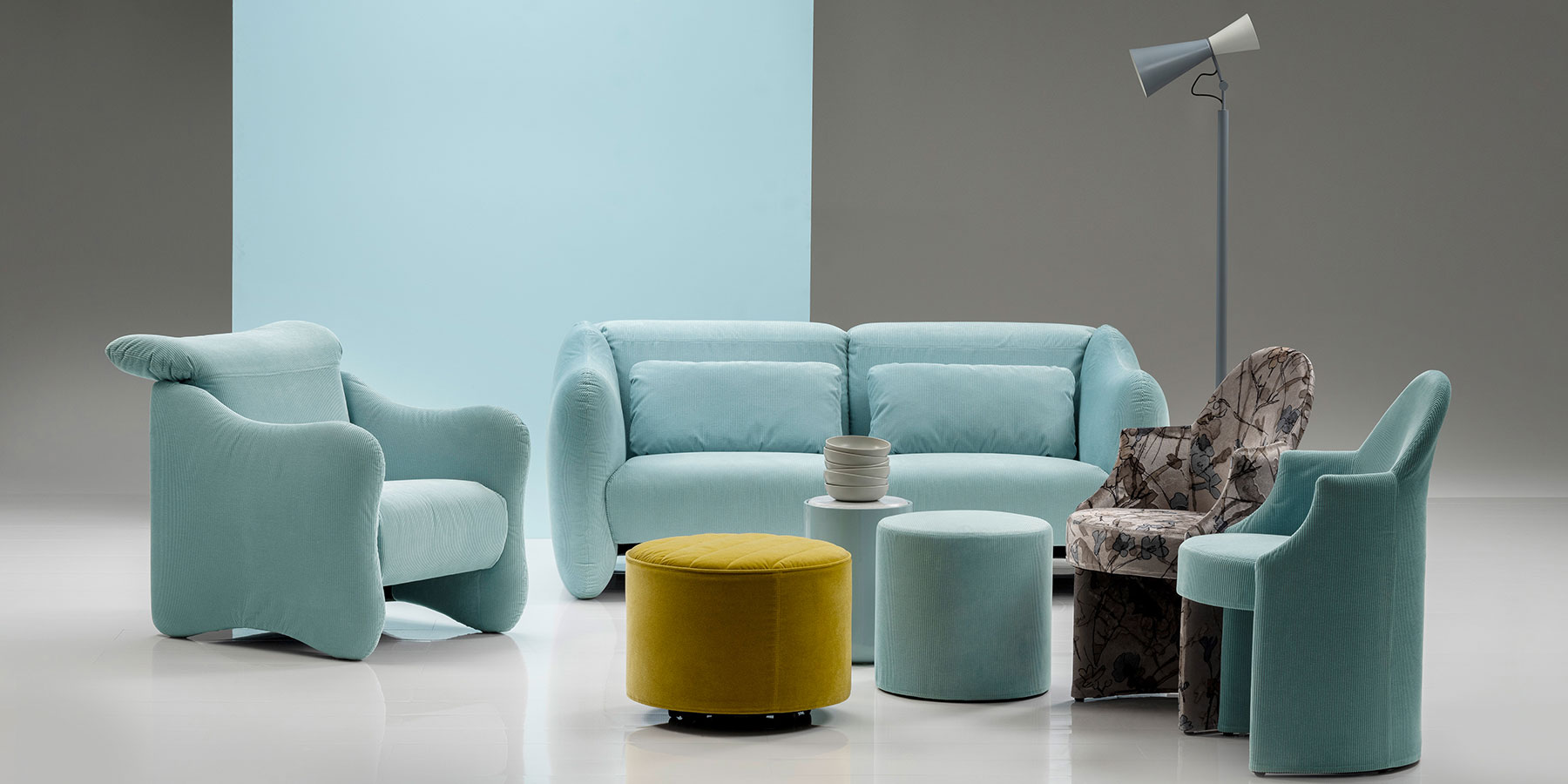 Ein Sessel und ein Sofa der Serie bongo bay von brühl stehen in einer Gruppe mit zwei weiteren Sesseln, zwei runden Hockern sowie einem zylindrischen Beistelltisch.