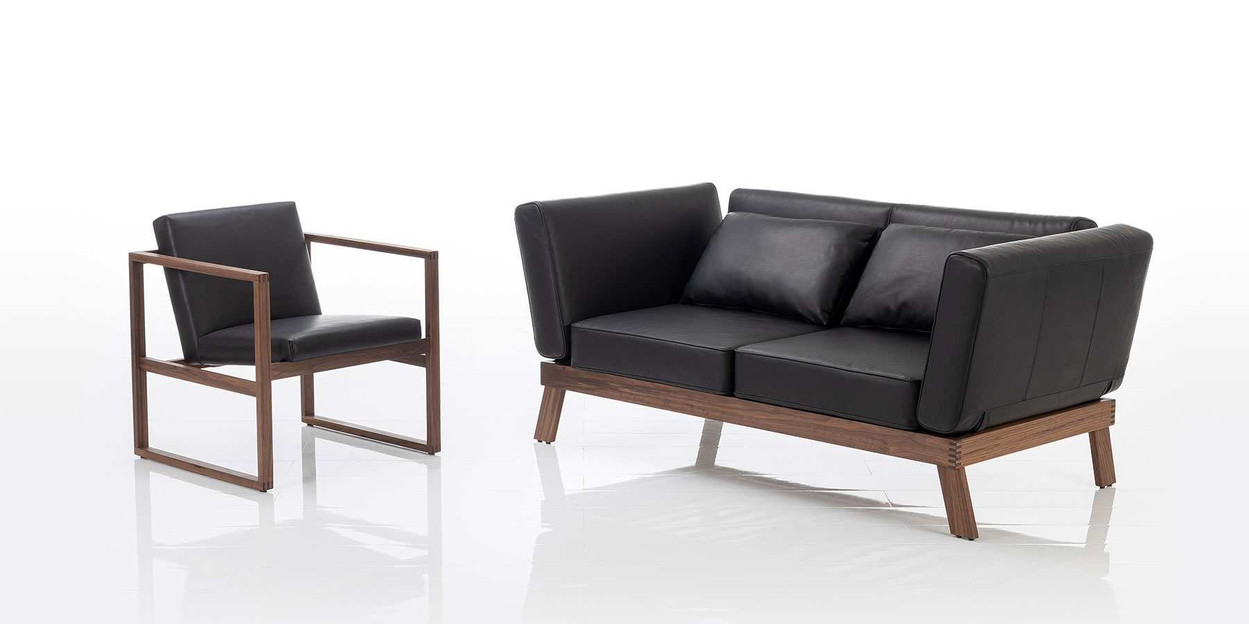 Sofas lofoten lounge Ein zweisitziges Sofa mit Holzgestell aus dunklem Holz. Die Polster sind mit schwarzem Leder bezogen.