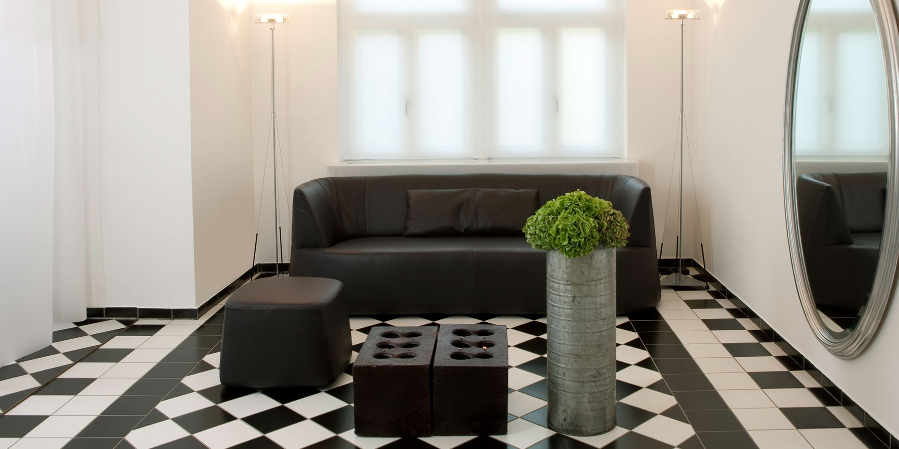 Sessel und Sofas brühl powder Ein schwarzes Ledersofa mit 3 Sitzen. Die Kontur ist A-förmig. Davor steht ein dazu passender schwarzer Lederhocker.
