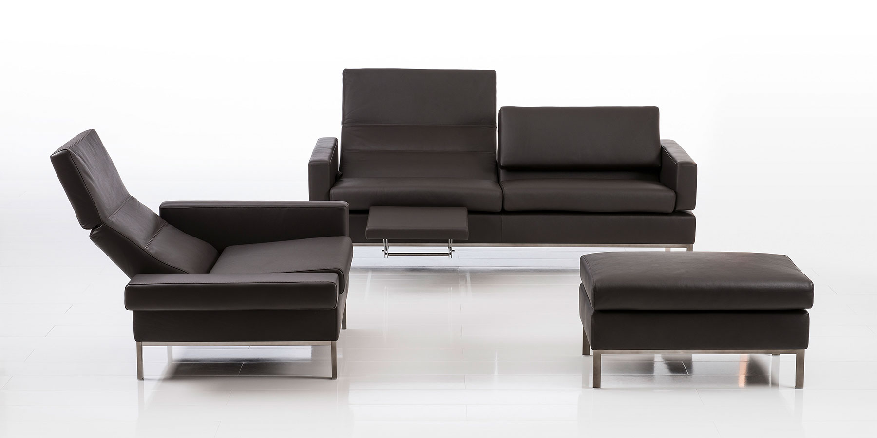 Sofas und Sessel brühl tomo compact Eine Polsterkombination bestehend aus einer 2-sitzigen Couchm einem Sessel mit abgesenkter Rückenlehne und einem Hocker in dunkelbraunem Leder.