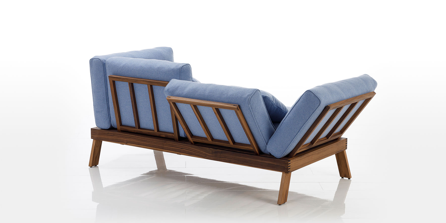 Sofas lofoten pure Ein zweisitziges Sofa steht mit dem Rücken zum Betrachter. Rücken und Seiten bestehen aus absenkbaren Holzelementen aus dunklem Eichenholz. Die hellblauen Rückenpolster sind auf diese aufgelegt.