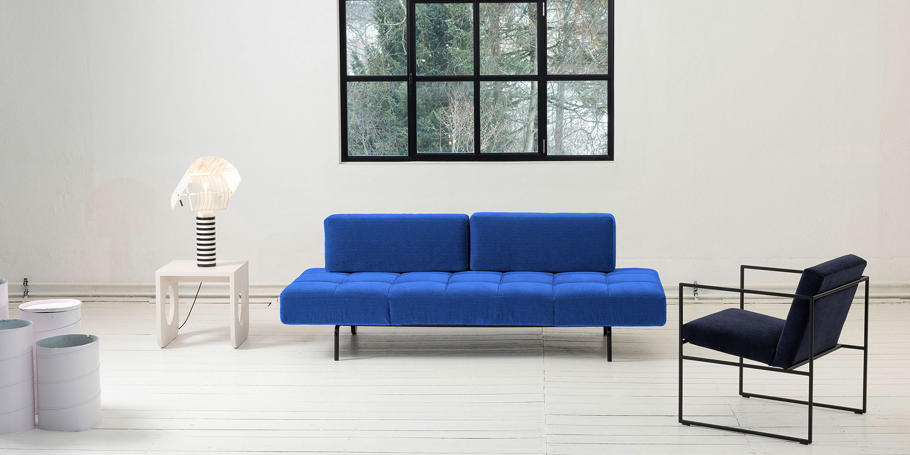 Schlafsofa brühl jerry Ein blaues Sofa ohne Armlehnen. Die Sitzfläche ist quadratisch gesteppt. Die zwei länglichen Lehnenpolster sind glatt gearbeitet und kürzer als die Sitzfläche. Das Metallgestell ist schwarz.