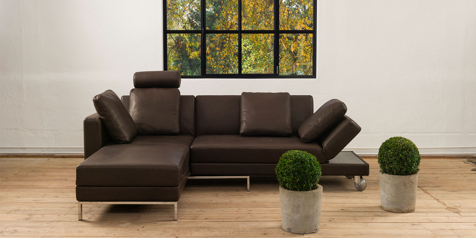 Multifunktionssofa four-two Eine Eckgarnitur in braunem Leder mit chromfarbenen Füßen. Links mit einem Openend, rechts mit einem Anstellsofa mit halb abgesenkter Armlehne.