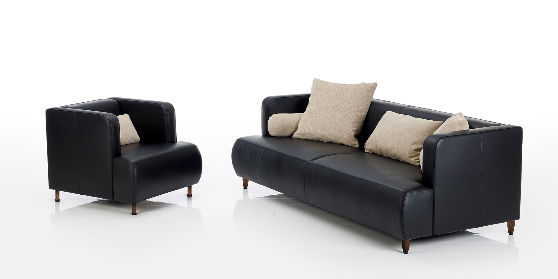 Sofas und Sessel von brühl aomyama Ein Ledersessel und eine Ledercouch von brühl aoyama aus schwarzem Leder mit Dekokissen in beige.