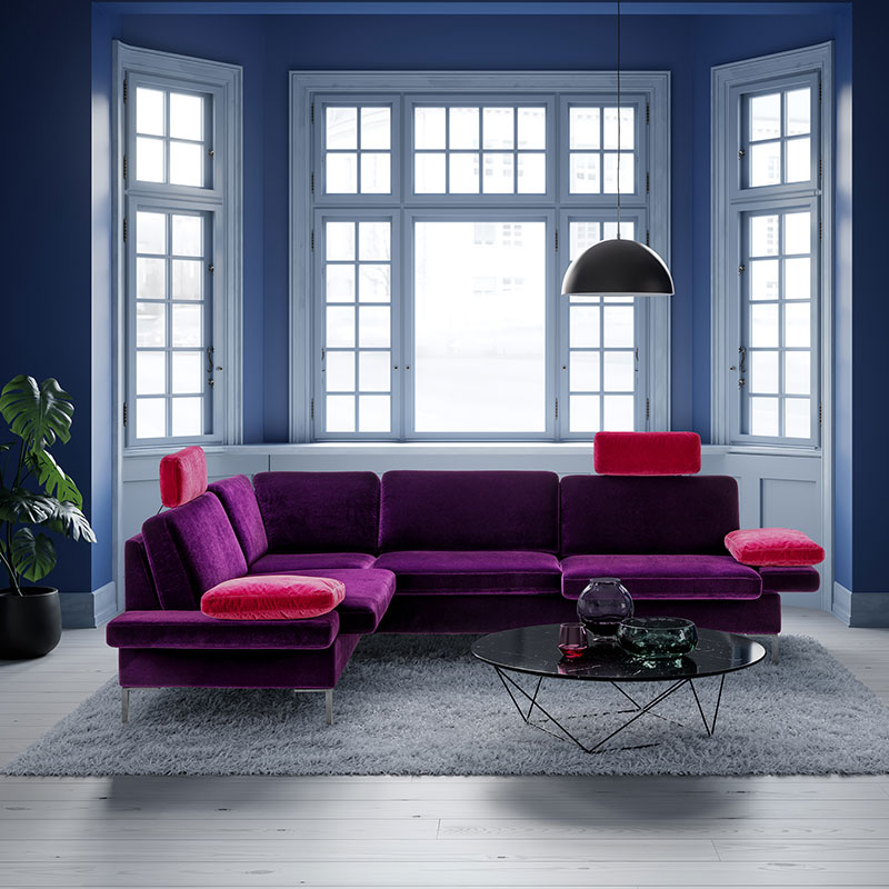 Link: brühl alba all in one Ambientebild mit lila-pinker Eckgarnitur vor einem großen Fenster.